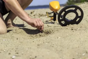 A man reaching into beach sand to retrieve a coin found with a metal detector.